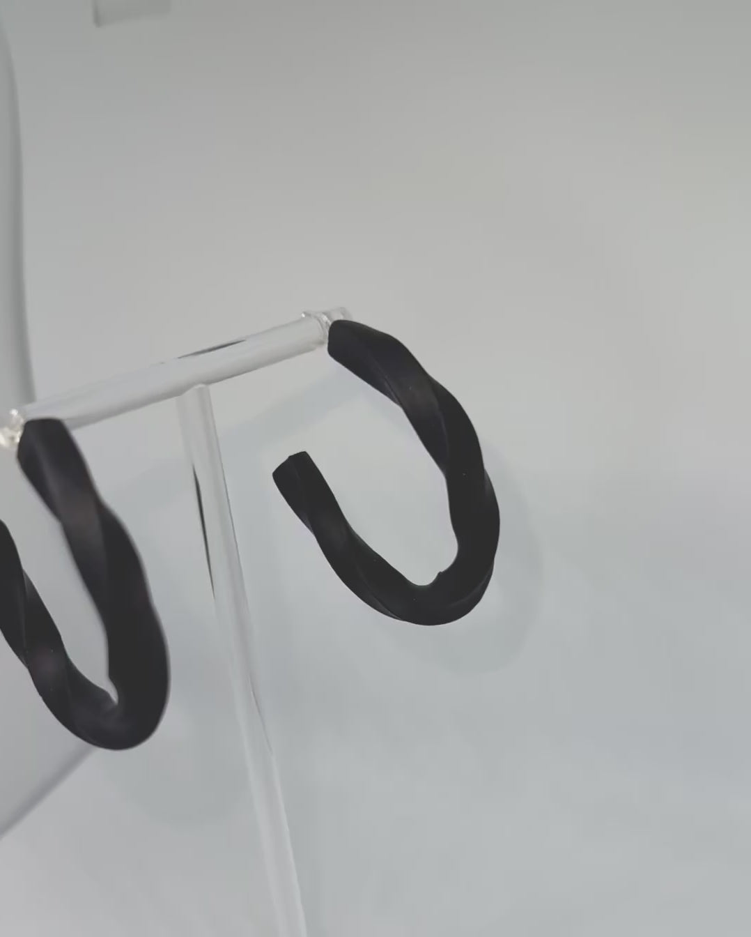 Black polymer clay twisted hoop earrings on a display stand – handmade bespoke earrings from an artisan jewellery store, part of a handcrafted clay jewellery collection perfect for gifting or everyday wearable art.