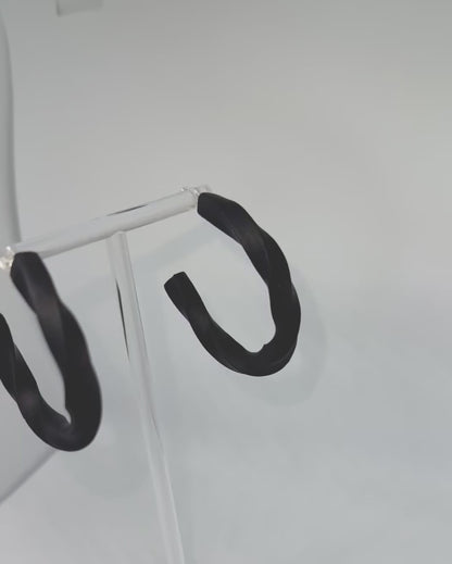 Black polymer clay twisted hoop earrings on a display stand – handmade bespoke earrings from an artisan jewellery store, part of a handcrafted clay jewellery collection perfect for gifting or everyday wearable art.